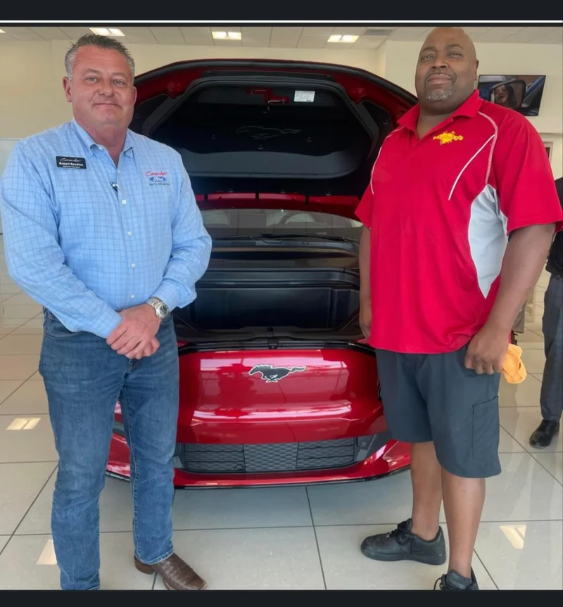 Detailer standing beside a red Mustang with its hood open